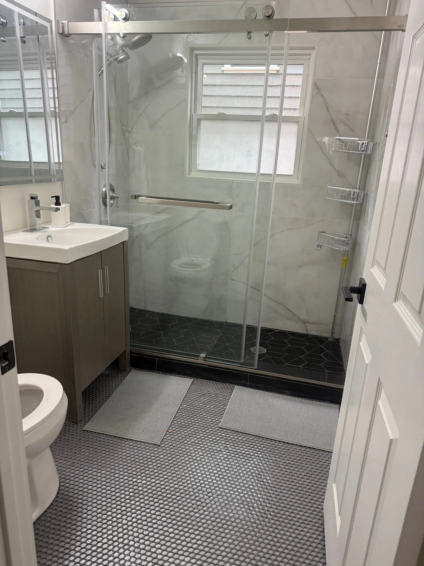 Completed bathroom renovation with glass shower enclosure, gray vanity, and geometric tile floor